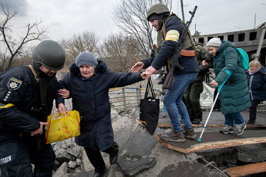 Police and militia forces help an elderly woman cross a destroyed bridge as residents of Irpin continue to try to evacuate the suburb, that has been heavily bombed by invading Russian forces, and get...