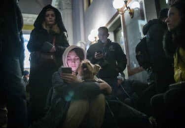 A young woman checks her mobile phone as she waits with her pet dog in the Central Ticket Hall at Lviv Grand Central Station. There are too many people queuing to get on to the platforms so people hav...