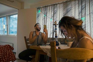 Omar (left) smokes a nargila and chats with his mother via video in Mary's (right) apartment. The two are both Syrians living in the same apartment block in
