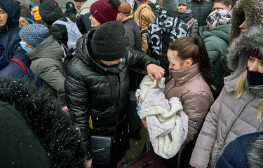 A young mother, holding her one-month-old baby, and her mother, standing next to her, wait with a huge crowd as the snow falls outside the station for the humanitarian train to Lviv. The family want t...