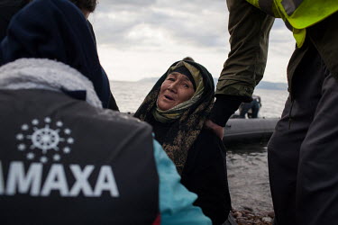 An elderly Afghan woman is helped off a dinghy by volunteers and other migrants and refugees travelling with her from Turkey.