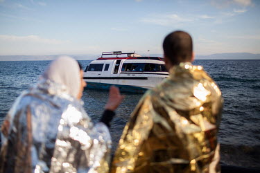 A pair of refugees, wrapped in space blankets, look at the boat in which they travelled from Turkey.