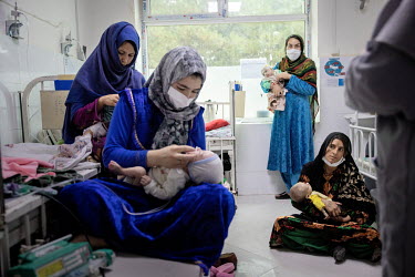 Fatemah with her baby girl Asheg (3 months) sit on the floor, surrounded by other mothers and their children, at the main hospital in Herat city where children suffering from severe acute malnutrition...
