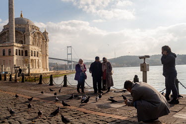 Foreign tourists take photos and feed the pigeons in front of the Ortakoy Mosque, with Istanbul's Asian shore in the background, during a nationwide weekend coronavirus curfew which didn't appear to a...
