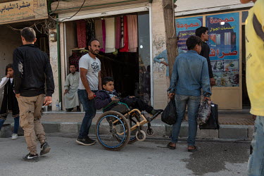 A man pushes a boy in a wheelchair on the main market street of Tel Abyad.