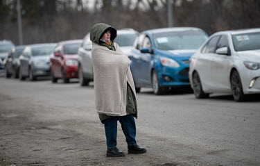 A woman wrapped in a blanket stands at the roadside beside a line of civilian cars, all heading eastward toward Kyiv. People trying to make their way into the capital are facing roadblocks and long qu...