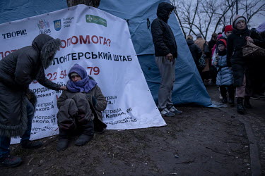 Veronica (32) sits, too exhausted to walk any further, on the cold ground outside the train station where a woman tries to encourage her to move inside a tent.  The station at Lviv is the main hub for...