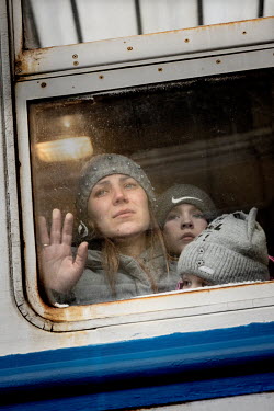 A woman, with her children, waves through the window of a train as it departs to Poland.  Under martial law, men aged 18 to 60 are not allowed to leave Ukraine, her husband, the children's father, is...