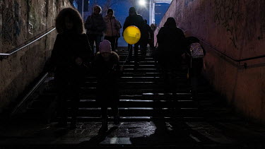 People, including a child carrying a McDonald's balloon, walk into a pedestrian underpass.