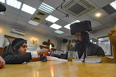 A Hasidic man and a youth pray and study in a synagogue.