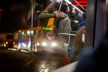 A young woman texting on her mobile phone in a public tram seen in a reflection of a window.