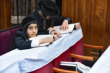 A Hasidic man and a youth pray and study in a synagogue.