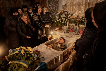 Oksana Ruschyshyn, holding her youngest child Roman, stands with her other children and close family beside the body of her husband inside their home during the funeral of the former police officer. R...