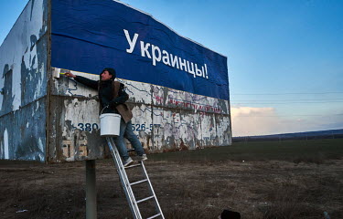 A man pasting a political poster on a billboard on a road near Dnipro.