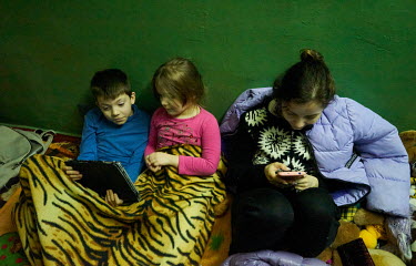 Three children look at their tablet and smartphone in the Kholodna Gora metro station where they have found shelter, with their family, after they fled shelling by Russian forces in the residential no...