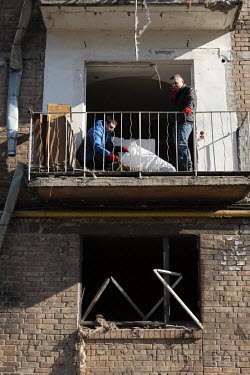 People clear debris from the balcony of a badly damaged residential apartment block, one of several civilian, residential areas of western Kiev that were targeted by Russian shelling over several days...