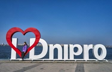 A young woman leaning on a heart, part of a giant 'I Love Dnipro' sign on Sicheslavska Naberezhna Street. People, mostly internally displaced persons (IDPs), enjoy the nice weather despite the sound o...