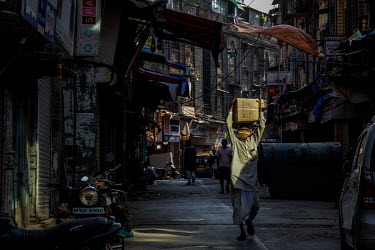 A day labourer carries a box of goods on an empty street close to the Mangal Das cloth market where all the non-essential goods shops were closed because of the second lockdown.