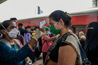 A health worker takes a woman's temperature and measures her oxygen saturation levels at the Dadar railway station while carrying out tests for COVID-19 on passengers arriving by train from outside th...