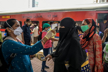 A health worker takes a woman's temperature and measures her oxygen saturation levels at the Dadar railway station while carrying out tests for COVID-19 on passengers arriving by train from outside th...