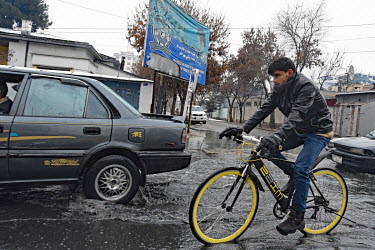 Traffic, including a man on a bicycle, on a flooded street on a rainy day in Kabul.