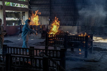 A funeral worker, in blue, performs the last rights for a man who died of COVID-19 and whose body is being cremated on a funeral pyre at the Hindu cremation ground on the outskirts of Mumbai.