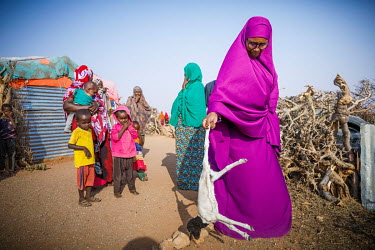 Local volunteer, Ibado (purple) holds a dead lamb, that died early in the day, while she talks with women outside their makeshift shelters while on her daily rounds visiting IDPs displaced by drought...