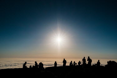 People watching from above the clouds as the sun descends towards the horizon and sunset approaches on Table Mountain.