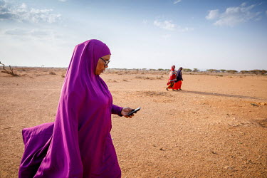 Local volunteer, Ibado (purple) checks her mobile phone while on her daily rounds visiting IDPs displaced by drought in a camp near Oog.