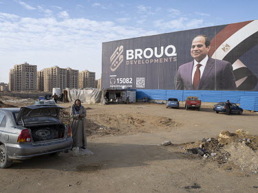 A man prays in front of a billboard featuring President al-Sisi on a roundabout in Egypt's New Administrative Capital.~Following persistent problems of overpopulation, pollution and traffic congestion...