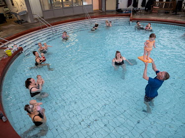 A group of women with their babies watch as Snorri Magnusson lets one of the children stand on his hands during a parent and child session in a swimming pool. Snorri Magnusson started giving swimming...