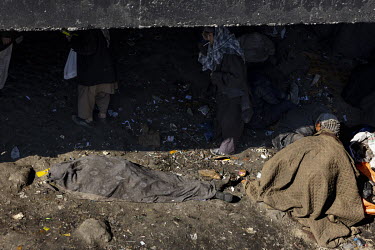 The body of a dead man lies on the ground beneath a bridge, covered by a blanket. He is one of seven drug users who gather in large numbers at that location who died that day.