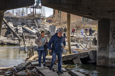Local civilians cross the River Irpin (Irpen) using planks that were laid beside the original bridge, connecting the commuter town to the capital, destroyed by Ukrainian defenders to prevent its use b...
