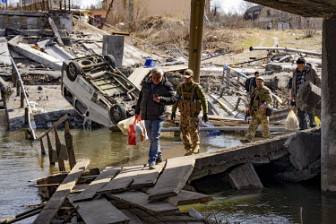 Civilians and soldiers cross the River Irpin (Irpen) via planks that were laid beside the original bridge, connecting the commuter town to the capital, destroyed by Ukrainian defenders to prevent its...