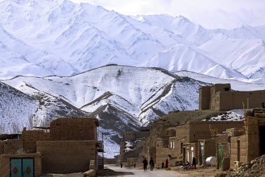 Snow covered mountains rise behind a village on the route between Kabul and Bamyan.