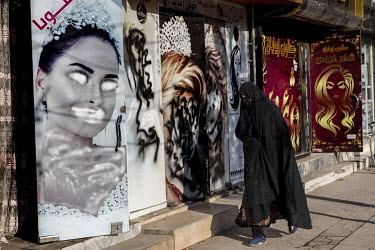 A veiled woman walks past a beauty salon where the images of women on its front have been defaced following the Taliban's take over.
