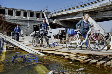 Local civilians push bicycles across the River Irpin (Irpen) using planks that were laid beside the original bridge, connecting the commuter town to the capital, destroyed by Ukrainian defenders to pr...