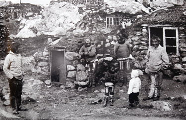 An old photograph of a group of Inuit outside their houses which were made of stone with a mud covering and insulated with grass.