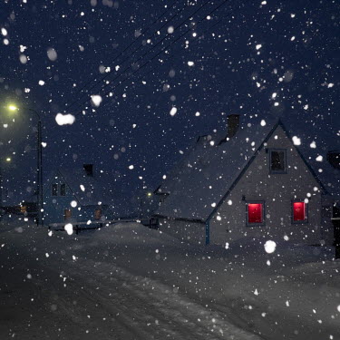 Lights illuminate the windows of a house during a winter snow flurry.