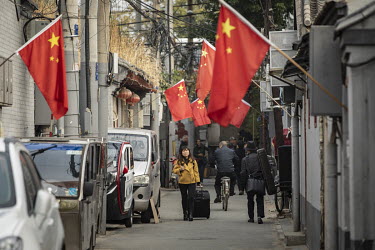 Pedestrians walk through an alley strewn with Chinese national flags.
