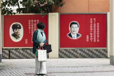 A woman stands in front of a poster of Chinese President Xi Jinping and legendary soldier Lei Feng at communist party affiliated office.