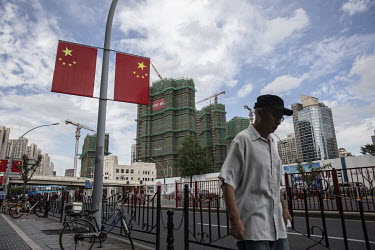 A man walks past Chinese national flags on display for the upcoming national day holiday near a housing construction site.