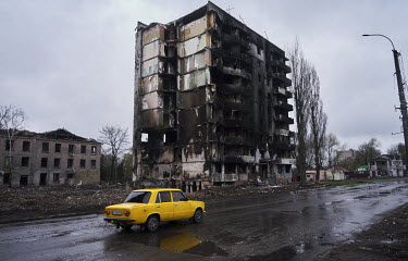 A car passes a destroyed apartment building burned, and blackened by flames, from Russian bombing.