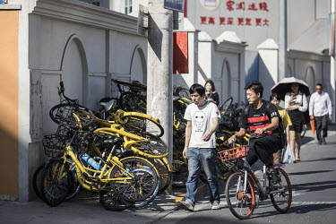 A pedestrian and a cyclist move past piles of shared bicycles from various providers. While cheap, convenient, and theoretically environmentally friendly, the craze and commercialisation of shared bik...