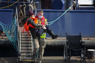 A person is carried ashore at Dover Harbour by a crew member from HMC Valiant after a group of migrants were picked up from the English Channel by the UK Border Force.