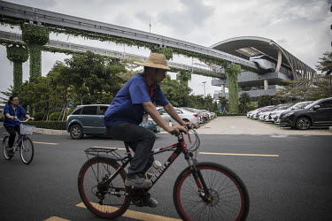 Employees riding bikes pass beneath the tracks of a prototype monorail train line which operates through the campus of BYD (Build Your Dreams) headquarters.