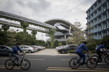 Employees riding bikes pass beneath the tracks of a prototype monorail train line which operates through the campus of BYD (Build Your Dreams) headquarters.