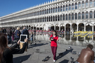 An Asian tourist photographed with a tablet, while feeding pigeons on Piazza San Marco. The famous square is at the lowest point in Venice and is consequently flooded during Acqua Alta or 'high water'...