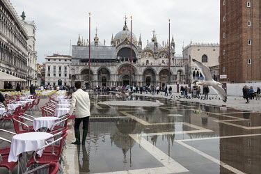 A waiter wearing Wellington (rubber) boots on a flooded cafe terrace in Piazza San Marco. The famous square is at the lowest point in Venice and is consequently flooded during Acqua Alta or 'high wate...