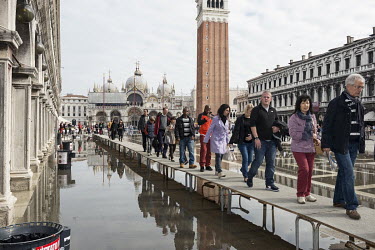 Tourists walking above flood water on running boards in Piazza San Marco. The famous square is at the lowest point in Venice and is consequently flooded during Acqua Alta or 'high water' from storm su...